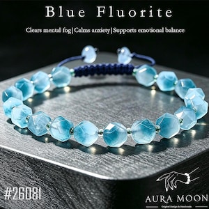 May include: A bracelet featuring faceted light blue fluorite beads separated by small metallic spacers. The bracelet has a dark blue adjustable cord closure with two small beads at the ends. Text on the image reads Blue Fluorite, #26081, and AURA MOON.