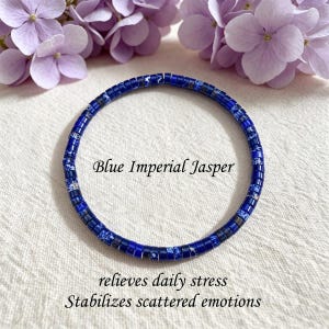 May include: A circular bracelet made of small, cylindrical blue imperial jasper beads with mottled white and dark blue patterns. The text Blue Imperial Jasper, relieves daily stress, and Stabilizes scattered emotions is printed near the bracelet.
