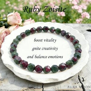 Puede incluir: Un collar de piedras preciosas de Rubí Zoisita con cuentas facetadas en tonos verdes y burdeos, exhibido en un plato blanco. La imagen incluye el texto "boost vitality, ignite creativity, and balance emotions."