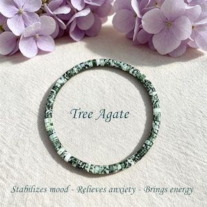 Könnte beinhalten: Ein kreisförmiges Armband aus kleinen, flachen, scheibenförmigen Baumachat-Perlen mit gesprenkelten grünen und weißen Mustern. Der Text Tree Agate steht in der Mitte, darunter der Text Stabilizes mood - Relieves anxiety - Brings energy.