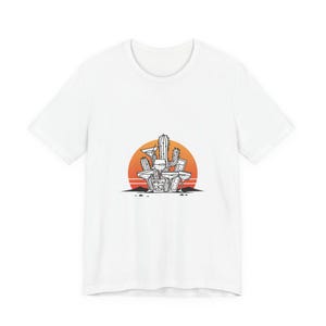 May include: White t-shirt featuring a graphic of cacti and a sunset. The design includes various cacti shapes in black and white, set against a vibrant orange and yellow sunset. The shirt is a casual wear item.