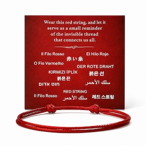 May include: A red string bracelet with a knotted closure is displayed in front of a red card. The card has text in multiple languages, including "Wear this red string, and let it serve as a small reminder of the invisible thread that connects us all."