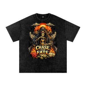 Op de afbeelding: Zwart t-shirt met een grafische afbeelding van een zeisdrager die een zandloper vasthoudt, met de tekst "CHASE YOUR FATE". Het ontwerp bevat dobbelstenen, geld en een skyline tegen een zonsondergang.
