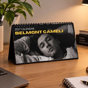 May include: A 2027 desk calendar with a black spiral binding featuring a black and white portrait of a person with dark hair. The text 2027 CALENDAR and BELMONT CAMELI are printed in white and yellow on the top portion of the calendar page.