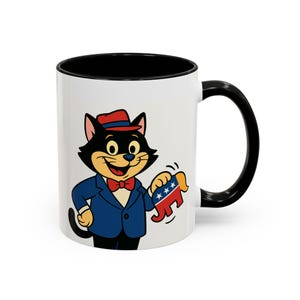 Può includere: Tazza in ceramica bianca con interno e manico neri. La tazza presenta un gatto dei cartoni animati con un abito blu, papillon e cappello rossi, che tiene un asino rosso, bianco e blu.