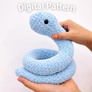 May include: A light blue crocheted snake toy with a black eye. The snake is held in two hands. The words "Digital Pattern" are in the top left corner.