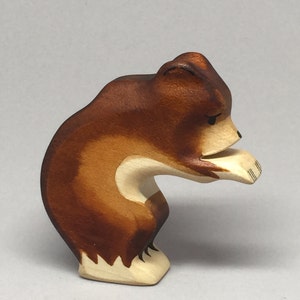May include: A wooden bear figurine with brown fur and white paws, standing on all fours with its head down as if sniffing the ground.