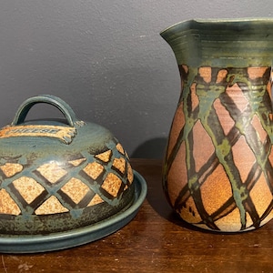 May include: A ceramic cheese dish with a lid and a matching pitcher. The cheese dish is teal with a lattice pattern and the word "CHEESE" on the lid. The pitcher is brown with green and teal accents.