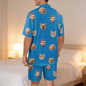 May include: A bright blue short-sleeve button-down shirt and matching shorts set featuring an all-over repeating pattern of various dog and cat faces, along with several human faces printed across the fabric in a scattered, uniform layout.