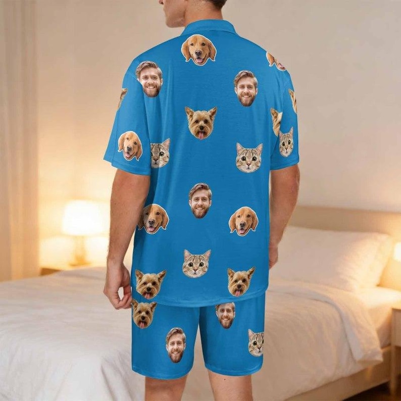May include: A bright blue short-sleeve button-down shirt and matching shorts set featuring an all-over repeating pattern of various dog and cat faces, along with several human faces printed across the fabric in a scattered, uniform layout.