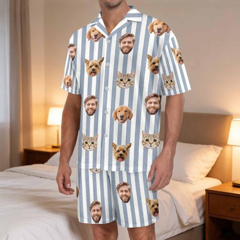 May include: A short-sleeved button-down shirt and matching shorts set featuring a vertical light blue and white striped pattern. The fabric is decorated with a repeating print of various dog and cat faces, along with the face of a bearded man.