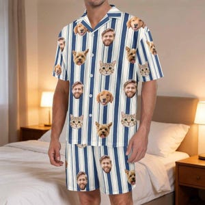 May include: A short-sleeve button-down shirt and matching shorts set featuring a vertical blue and white striped pattern. The fabric is decorated with a repeating print of various dog faces, cat faces, and a man's face scattered across the garment.