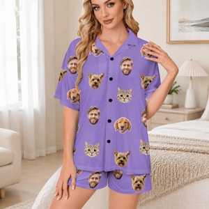 May include: A purple short-sleeve button-down pajama shirt and matching shorts set featuring an all-over print of various dog faces, cat faces, and human faces. The garment has a notched collar, a front button closure, and a relaxed fit.