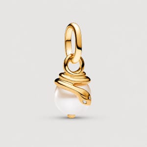 Pode incluir: Um pingente dourado com uma pérola branca redonda e lisa envolta por um design de cobra estilizada. O corpo da cobra é feito de metal dourado polido, com duas pequenas pedras transparentes como olhos na cabeça e uma argola circular no topo.