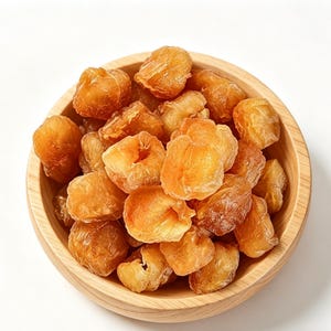 May include: A wooden bowl brimming with dried longan fruit. The fruit is a golden-brown hue with a textured, wrinkled appearance. The bowl is crafted from light-coloured wood and rests on a white surface. The image is well-lit, showcasing the details of the fruit.