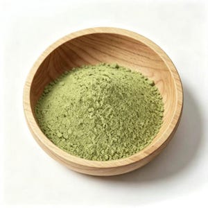Puede incluir: Un cuenco redondo de madera de color marrón claro lleno de un montón de polvo fino de color verde pálido. El cuenco presenta un patrón de veta de madera visible en todo su interior y exterior, conteniendo la sustancia verde seca y texturizada.