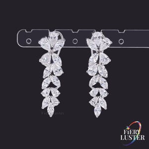 May include: A pair of silver-toned drop earrings featuring a vertical arrangement of marquise and pear-cut clear stones in a leaf-like pattern. The earrings are attached to a clear plastic display card with the text Fiery Luster visible at the bottom.