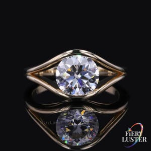 May include: A gold ring with a large, round, clear diamond. The diamond is the focal point, set in a unique, open-style band. The ring is displayed on a reflective black surface, showcasing its brilliance.