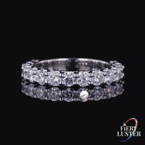 May include: A silver-toned eternity band ring featuring a continuous row of round, clear, faceted stones set in a metallic frame. The ring is displayed against a dark background, with a reflection visible beneath it and the text Fiery Luster.