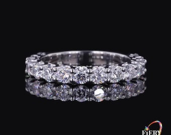 May include: A silver-toned eternity band ring featuring a continuous row of round, clear, faceted stones set in a metallic frame. The ring is displayed against a dark background, with a reflection visible beneath it and the text Fiery Luster.
