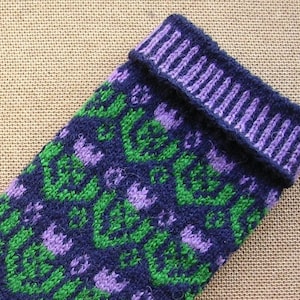 May include: A close-up of a knitted sock with a purple, green, and blue pattern. The sock has a folded-over cuff.