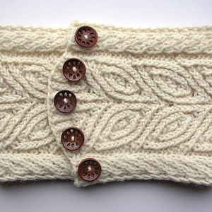 May include: A white knitted headband with a leaf pattern and five brown wooden buttons.