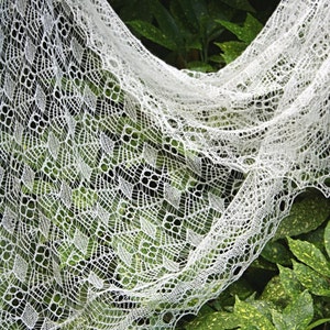 May include: A white lace shawl with a delicate pattern, draped over green leaves.