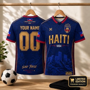 May include: Two blue soccer jerseys with red trim and gold accents. The front features the text HAITI, 1804, and a crest. The back displays YOUR NAME, 00, and SAK PASE. Both shirts include the Haitian flag, palm tree graphics, and architectural motifs.