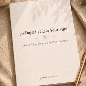 Könnte beinhalten: Ein Buch mit dem Titel "30 Days to Clear Your Mind" und dem Untertitel "A Calming Reset for Women Who Think Too Much". Das Buch liegt offen auf einer beigen Oberfläche mit einem goldenen Stift und einer Kaffeetasse.