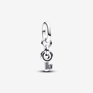 May include: A polished sterling silver charm shaped like a small key, featuring a circular head with a central cutout and a short, rectangular bit. The charm hangs from a smooth, oval-shaped jump ring, designed to be attached to a bracelet or necklace.