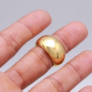 May include: A polished gold-tone dome ring with a smooth, reflective surface. The ring features a wide, rounded band design that sits prominently on the finger, showcasing a high-shine metallic finish that catches the light across its curved exterior.