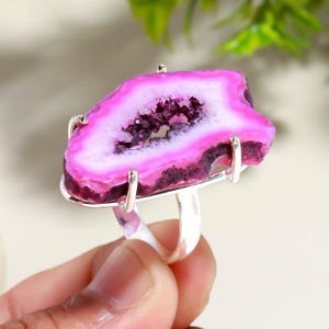 May include: A silver ring with a striking pink and white agate stone. The stone has a crystalline centre and a polished, irregular shape. The ring's setting is a simple, modern design, highlighting the natural beauty of the gemstone.