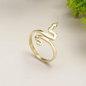 Peut inclure: Une bague dorée en forme de serpent. Le corps du serpent s'enroule autour du doigt, la tête relevée. La bague est en métal brillant et a une surface lisse. C'est un bijou.
