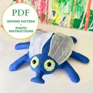May include: A blue fabric insect plush toy with translucent white wings featuring green stitching, black button eyes with green fabric borders, and a snout. A circular graphic includes the text PDF SEWING PATTERN + PHOTO INSTRUCTIONS.