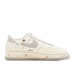 Pu&ograve; includere: Sneakers Nike Air Force 1 color crema con uno swoosh grigio e suola maculata. La scarpa presenta il testo "JUST DO IT" su un'etichetta e "Woodstock" in corsivo rosso. &Egrave; visibile anche una piccola grafica.
