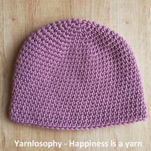 May include: A close-up of a crocheted beanie in a dusty rose color. The beanie is made with a textured stitch and has a simple, rounded shape.