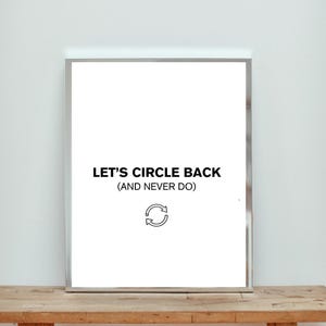May include: A framed white print with the text "LET'S CIRCLE BACK (AND NEVER DO)" in black, along with a circular arrow symbol. The frame is silver, and the print is displayed on a wooden surface.