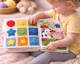 May include: A handmade crochet activity book for toddlers. The book features colorful squares with various shapes and textures, including a red circle, blue star, and yellow flower. The second page shows a cow, flowers, and a pig. The book is open, and a child is interacting with it.