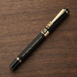 Op de afbeelding: Een zwarte en gouden vulpen met de tekst "Laser engraving customization area". De pen heeft gouden accenten, een decoratief draakembleem en een getextureerde grip. Ligt op een houten oppervlak.