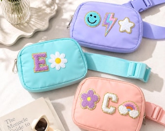 May include: Three rectangular belt bags in light purple, turquoise, and peach. The purple bag features a smiley face, lightning bolt, and star patch. The turquoise bag has a letter E and daisy patch. The peach bag has a flower, letter C, and rainbow.