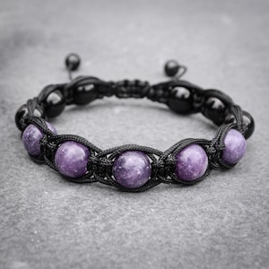May include: Black macramé bracelet with six purple gemstone beads and black accent beads. The bracelet has an adjustable sliding knot closure. The gemstones are a vibrant purple colour.