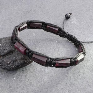 May include: A bracelet featuring dark red, rectangular, polished gemstone beads secured within a black woven cord. The design includes a sliding knot closure with a single black bead at the end of the adjustable cord, creating a flexible structure.