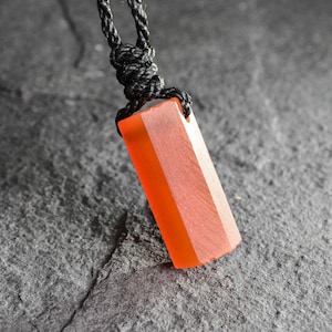 May include: Orange rectangular pendant necklace with a black cord. The pendant has a faceted design and is suspended from a knotted black cord. The pendant's color is a vibrant orange.