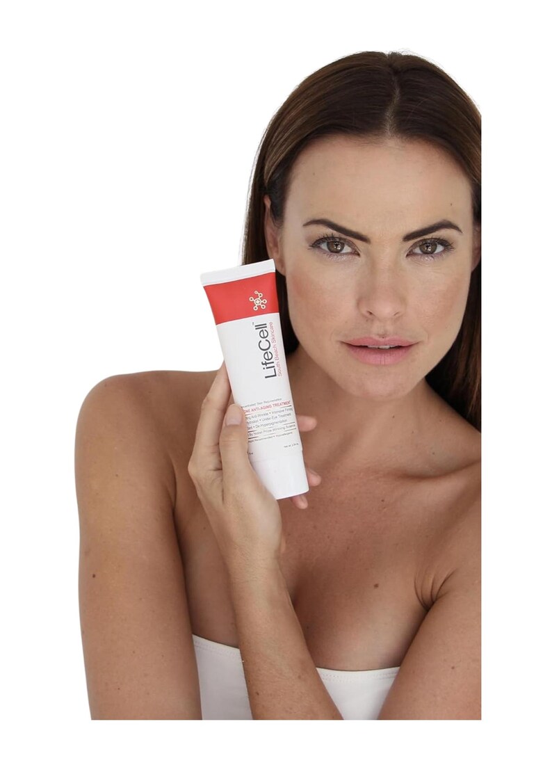 May include: A white squeeze tube of LifeCell anti-aging treatment with a red band at the top. The product label features the brand name LifeCell in black text, a small molecular icon, and additional descriptive text printed in black.