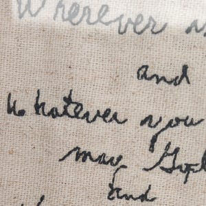 May include: Close-up of a beige fabric with handwritten text in black and gray ink. The text includes the words "Wherever" and "Whatever" in a cursive script. The fabric has a woven texture.