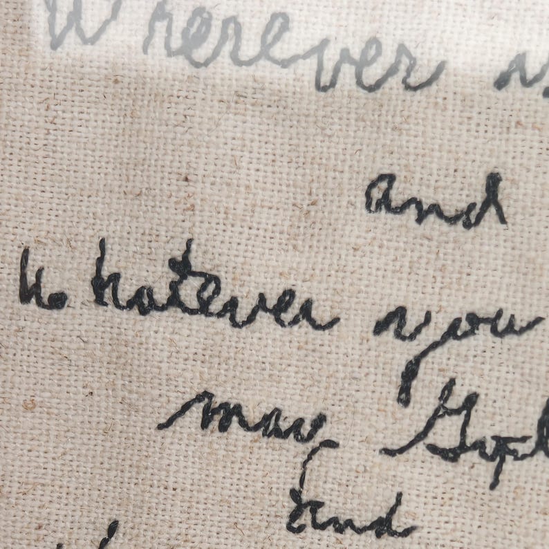 May include: Close-up of a beige fabric with handwritten text in black and gray ink. The text includes the words "Wherever" and "Whatever" in a cursive script. The fabric has a woven texture.