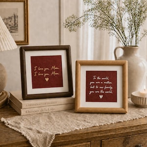 May include: Two framed prints with heartfelt messages. One, in a dark brown frame, reads "I love you, Mom. I love you, Mum." The other, in a light brown frame, says "To the world, you are a mother, but to our family, you are the world."