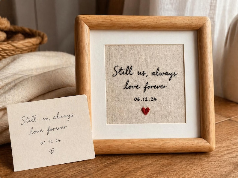 May include: A framed artwork with the text "Still us, always love forever" and the date 06.12.24, along with a small embroidered red heart. A matching card with the same text and a heart is also present.