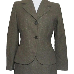 May include: A two-piece olive green suit. The suit includes a blazer with two black buttons and a matching skirt. The fabric has a subtle speckled texture. The suit is displayed on a mannequin.