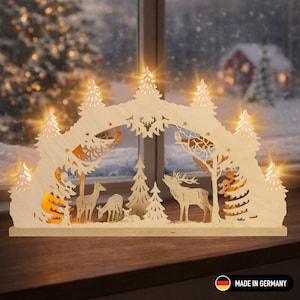 Op de afbeelding: Houten kerstdecoratie met een bosscène met herten en bomen, verlicht door warme LED-lampjes. Het ontwerp bevat uitgesneden details en een besneeuwde achtergrond, waardoor een feestelijke sfeer ontstaat. De basis is gemaakt van lichtgekleurd hout.